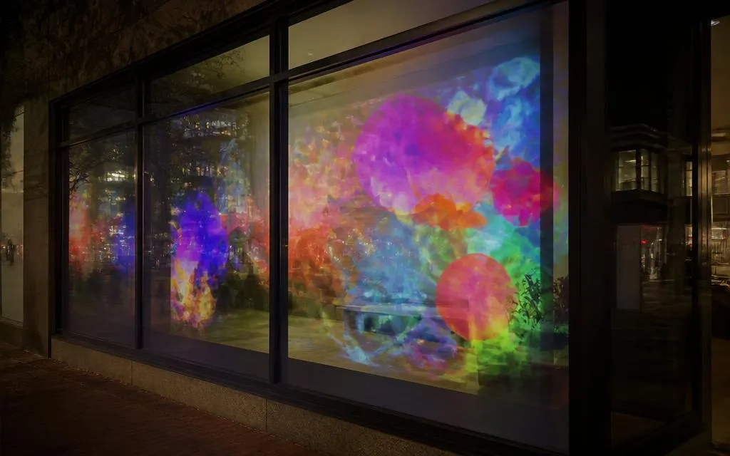 Colourful projected graphics cast onto a storefront window at night, viewed from the sidewalk